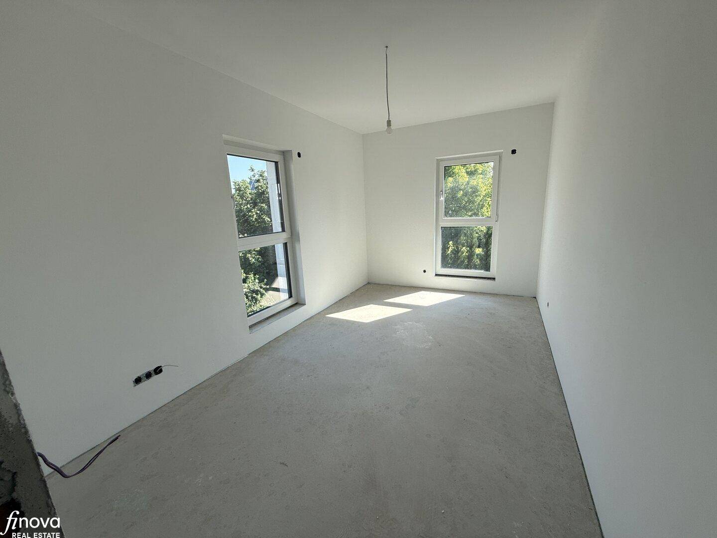 Helles Schlafzimmer im Rohbau mit zwei Fenstern und Blick ins Grüne.
