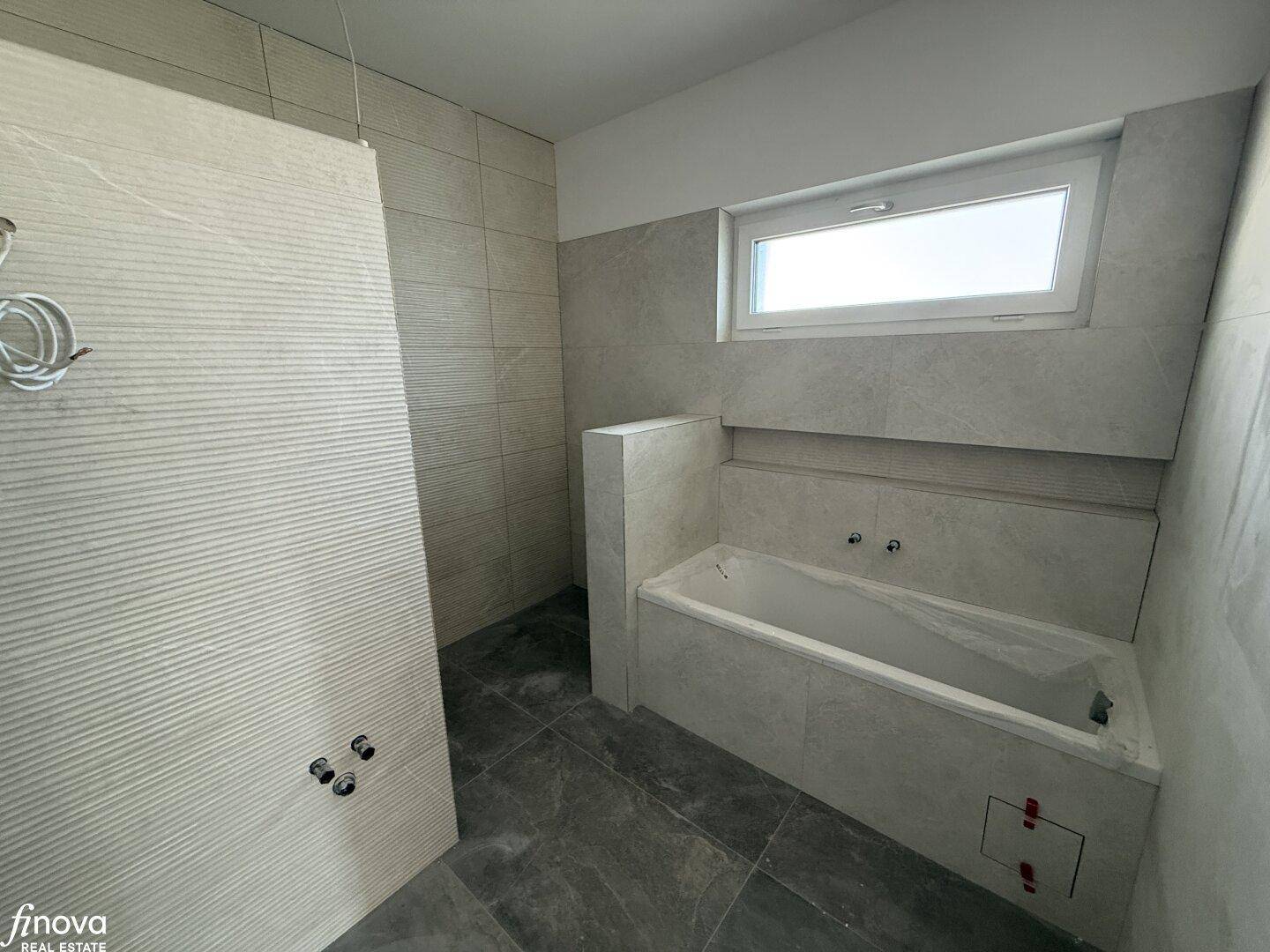 Modernes Badezimmer im Rohbau mit Badewanne und Fenster, bereit für die Fertigstellung.
