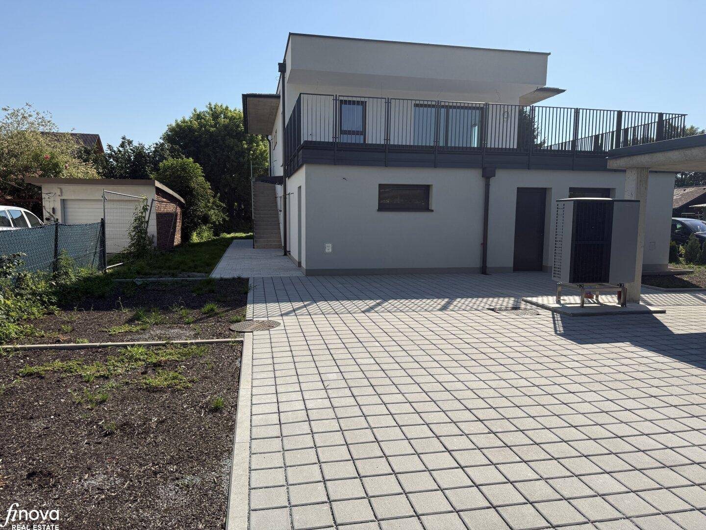 Neubau-Doppelhaushälfte mit modernem Design, gepflastertem Bereich und Außentreppe zum Eingang.