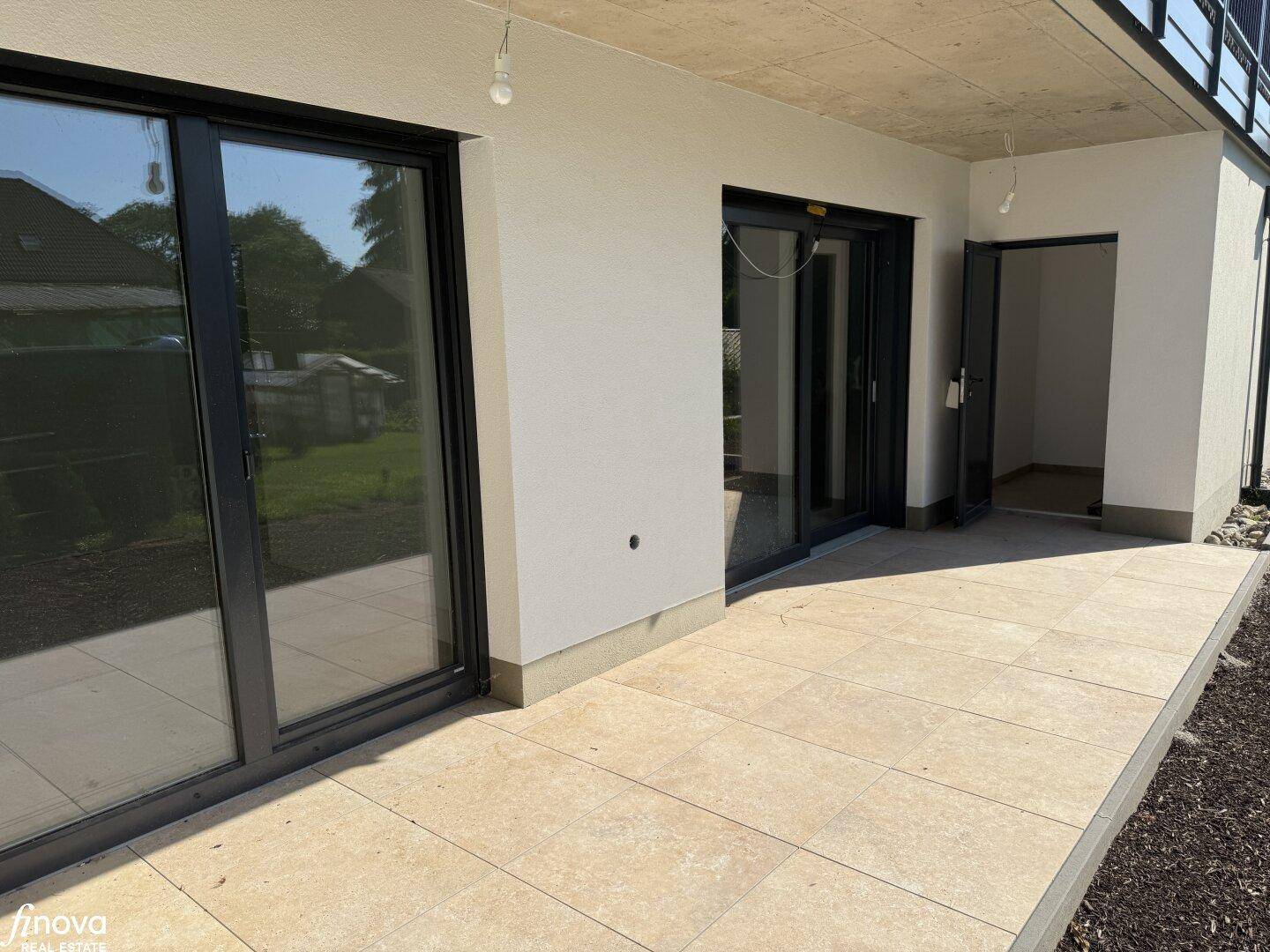Großzügige, geflieste Terrasse mit breiten Glasschiebetüren zum Innenbereich und Blick ins Grüne.