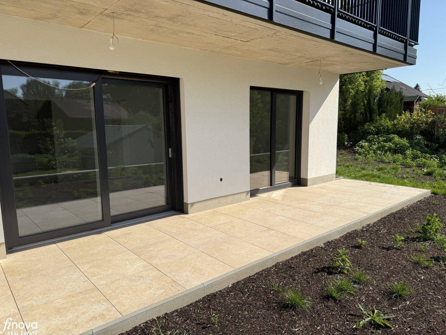 Helle, geflieste Terrasse mit Zugang zum Garten und großen Fenstern, die viel Licht hereinlassen.