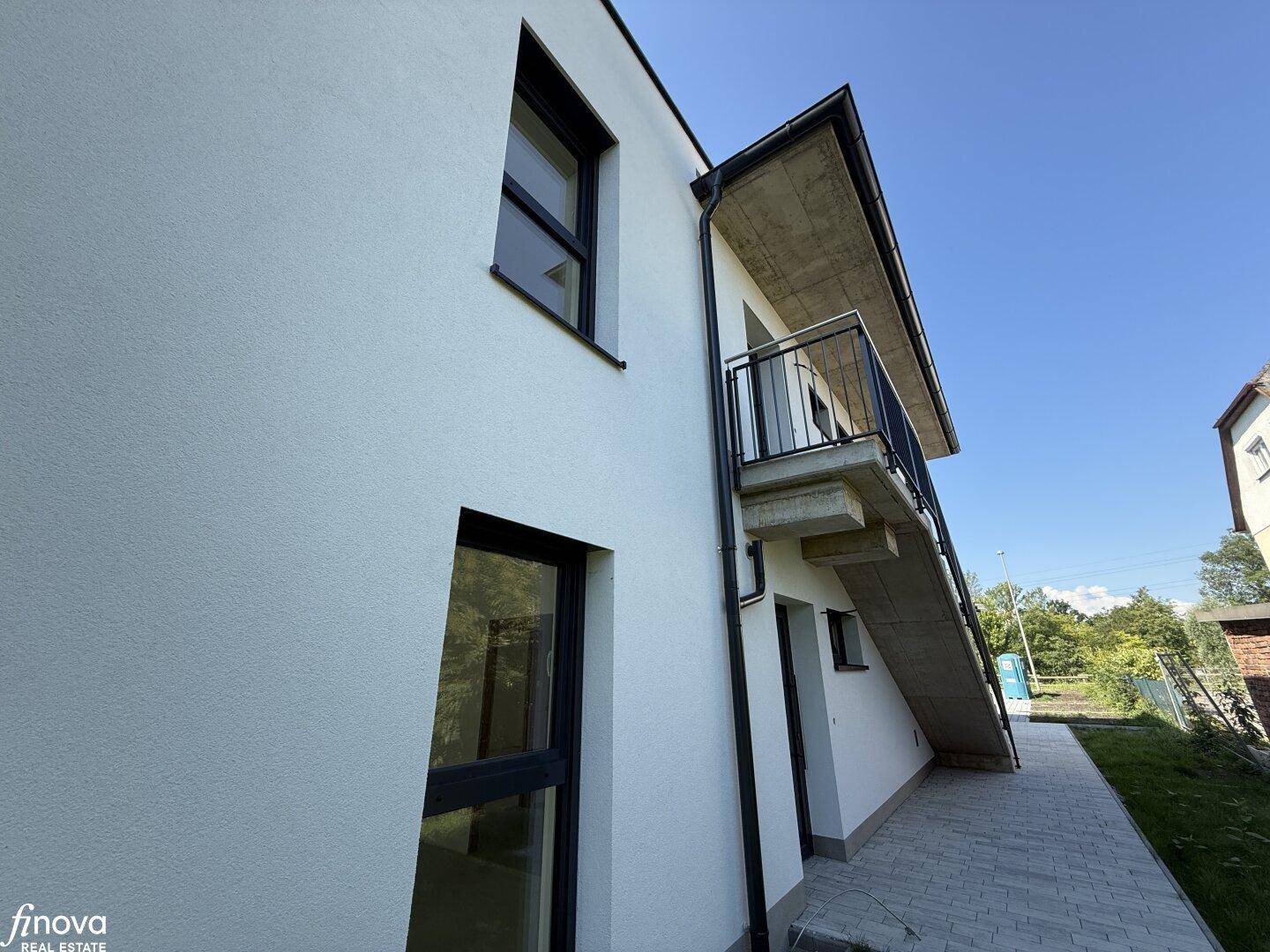 Seitenansicht der modernen Gebäudefassade mit dunklen Fensterrahmen und einem Balkon im Obergeschoss.