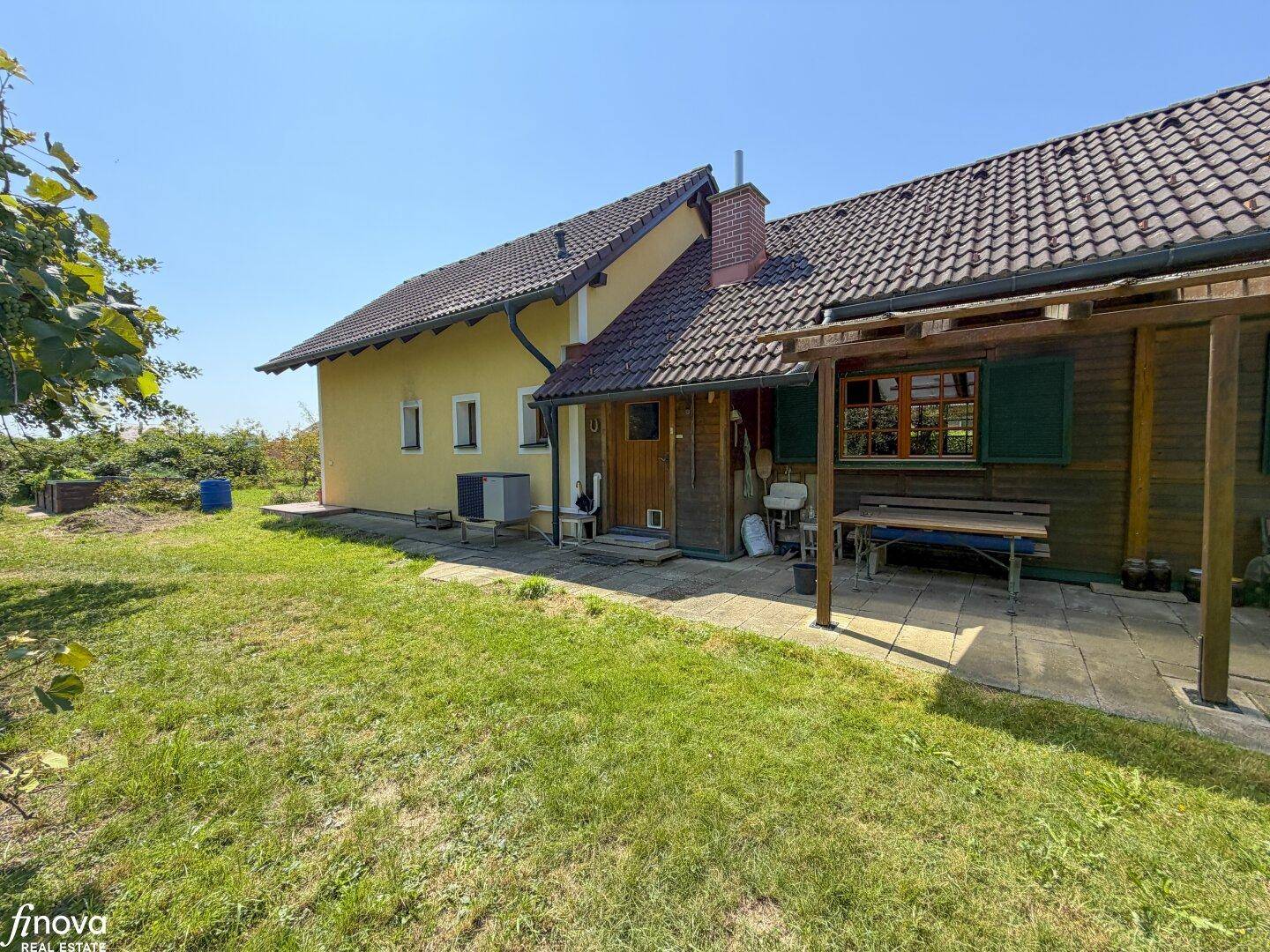 Seitlicher Blick auf das Haus mit überdachter Terrasse und Sitzgelegenheit im Grünen.