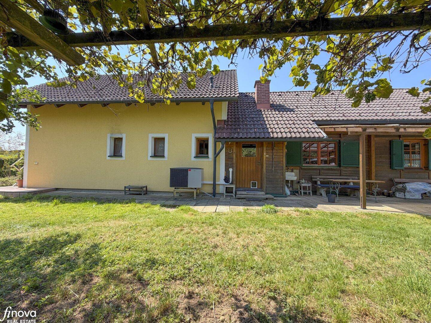 Ansicht des Hauses von der Seite mit einer überdachten Terrasse und viel Grünfläche.