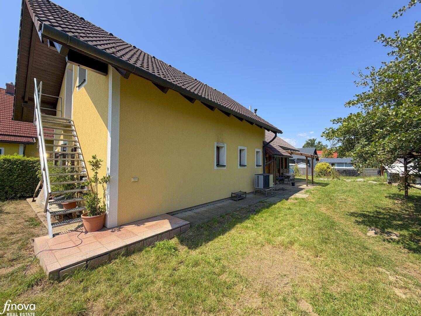 Seitenansicht des Hauses mit gelber Fassade, Außentreppe und Zugang zum oberen Stockwerk.