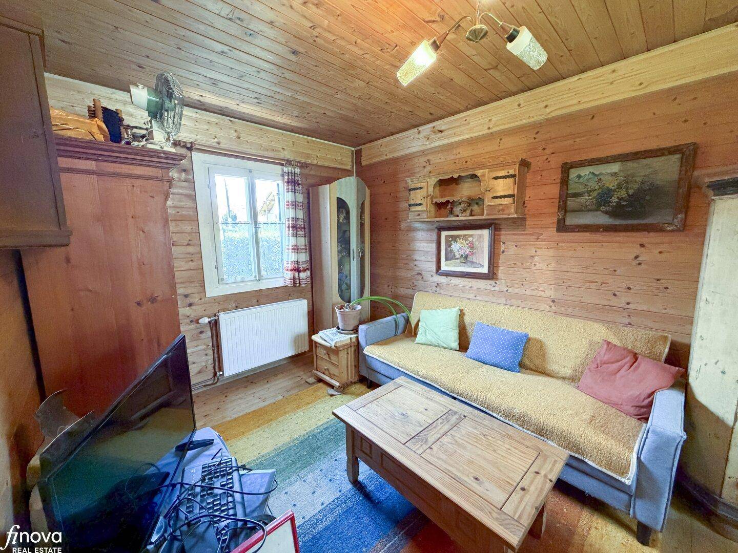 Rustikales Wohnzimmer mit Holzvertäfelung, Sofa und Teppichboden in warmen Farben.