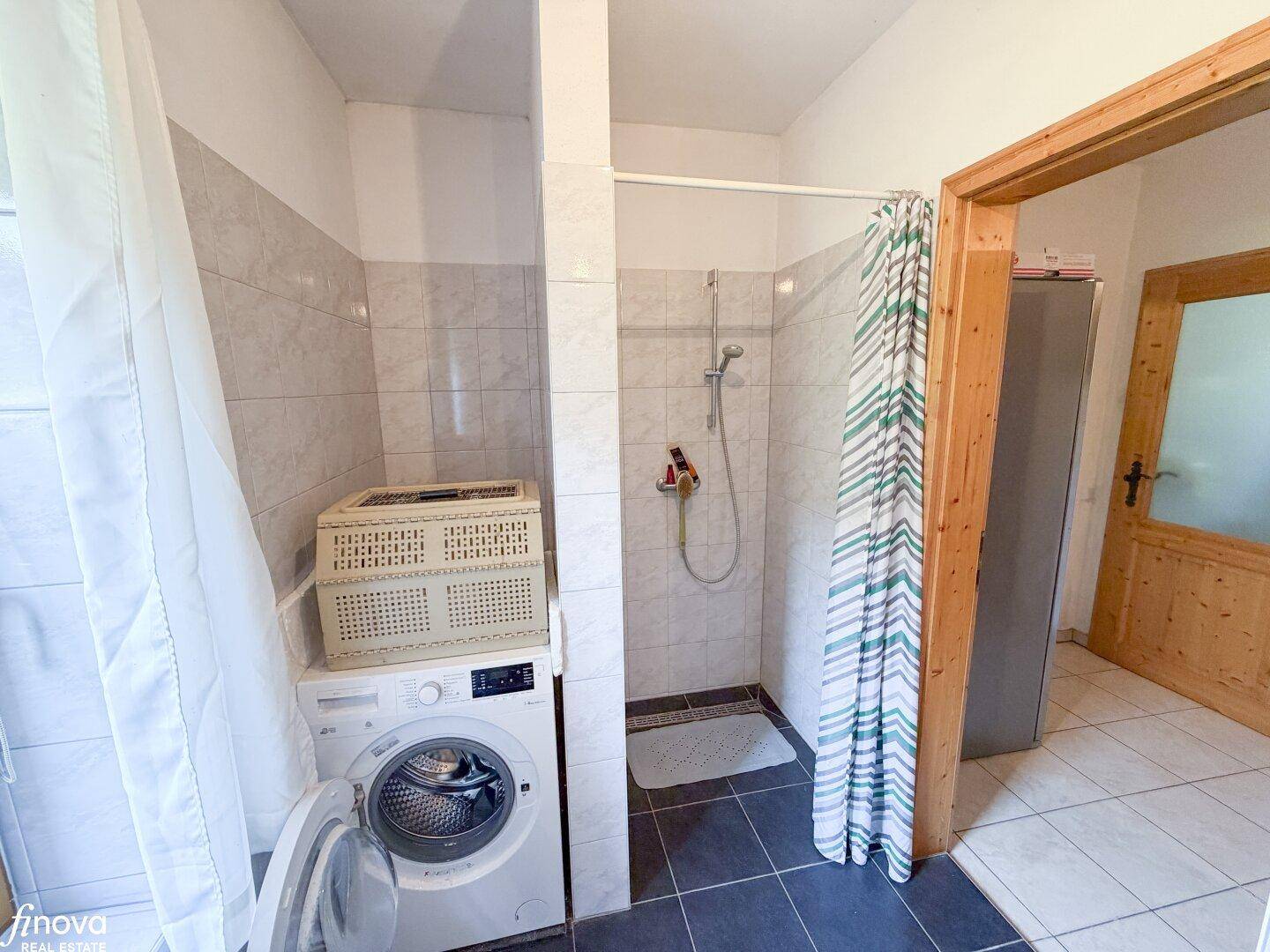 Badezimmer mit Duschbereich, Waschmaschine und Fliesen an Wänden und Boden.