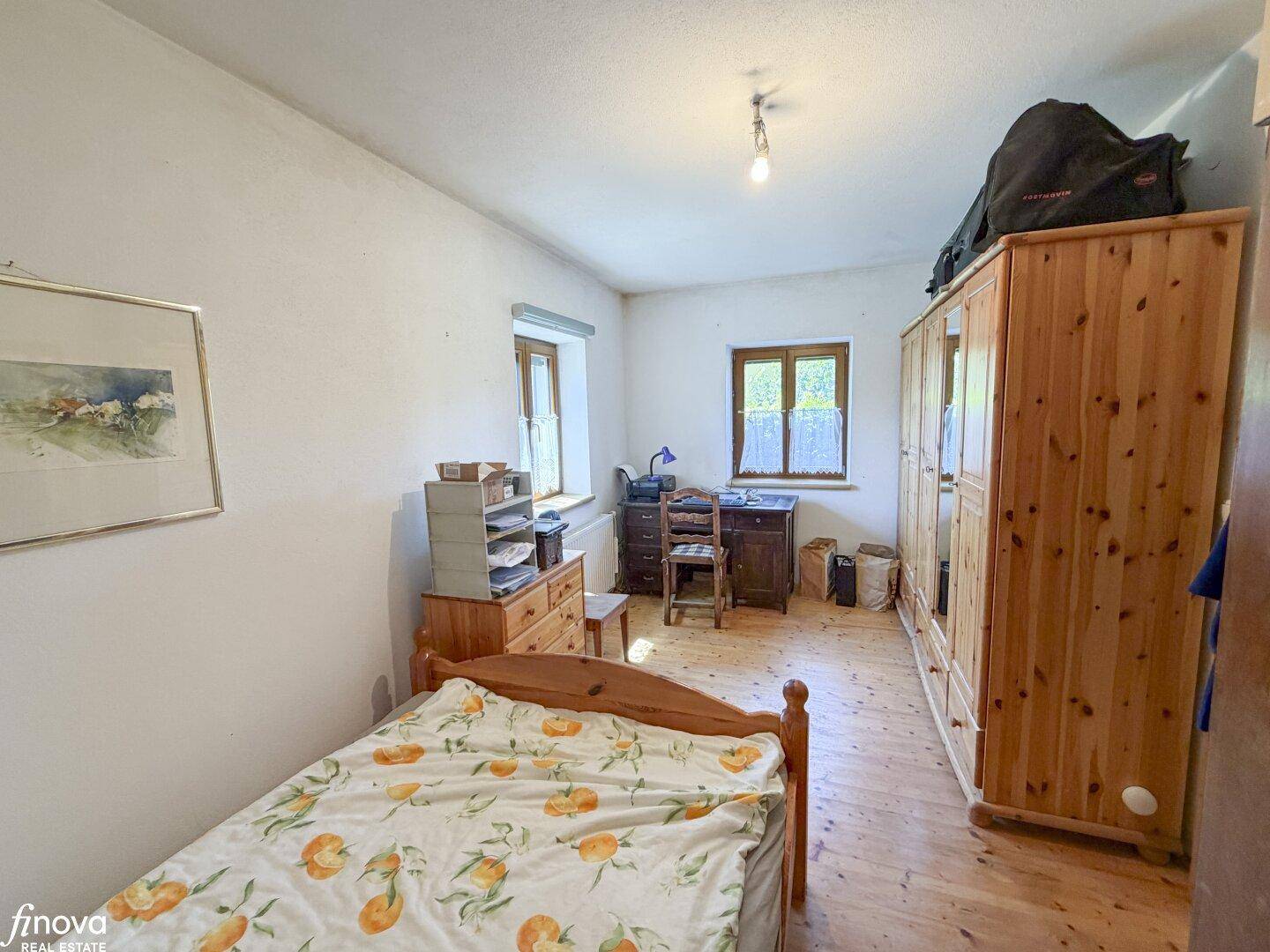 Helles Schlafzimmer mit Holzboden, Holzmöbeln und zwei Fenstern.