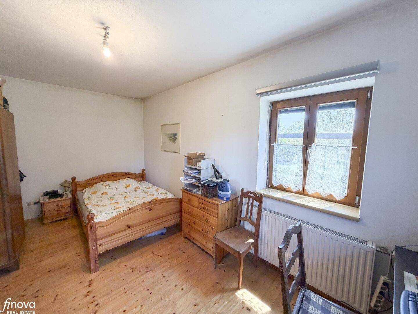 Gemütliches Schlafzimmer mit Holzboden, Einzelbett und Fenster mit Blick ins Grüne.