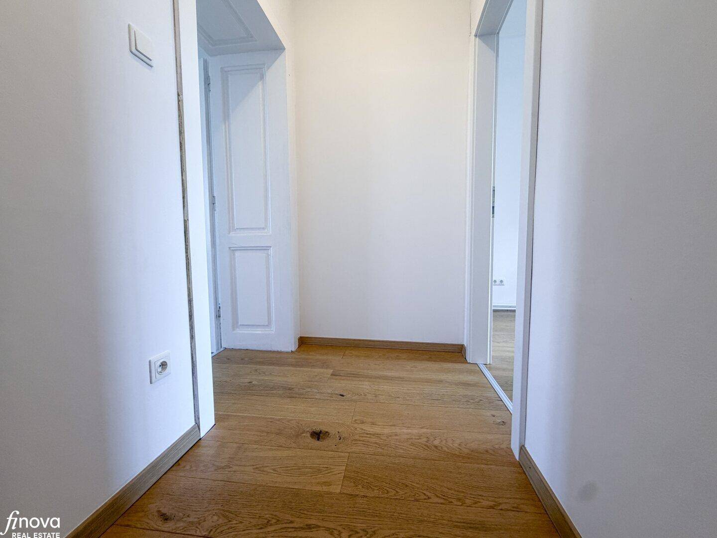 Heller Flur mit Holzboden und Zugang zu verschiedenen Zimmern, schlicht und funktional.