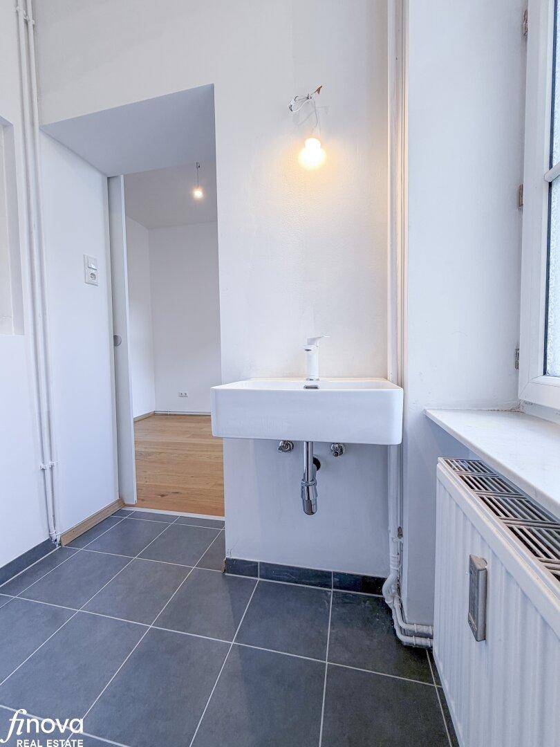 Badezimmer mit modernem Waschbecken und grauen Bodenfliesen, bietet Zugang zu einem weiteren Raum.