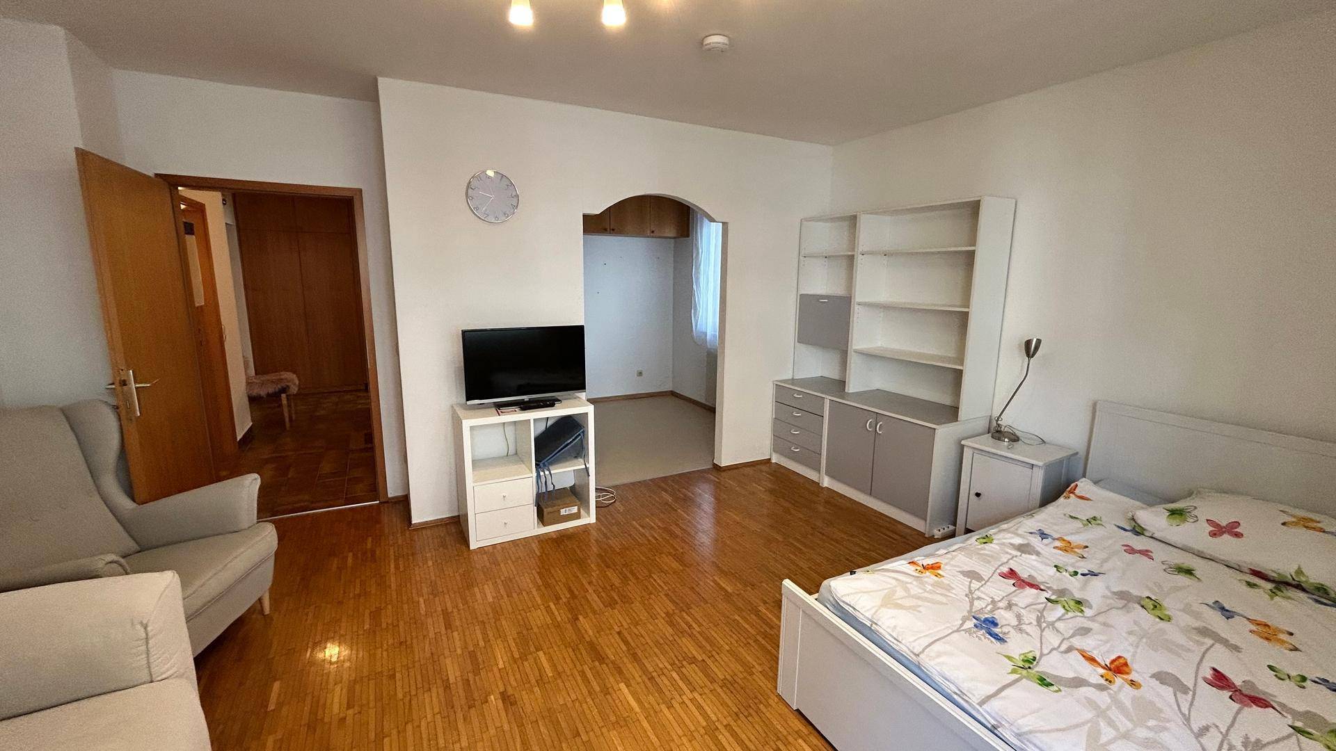 Geräumiges Wohnzimmer mit Parkettboden, Schlafbereich und Durchgang zu einem weiteren Raum.