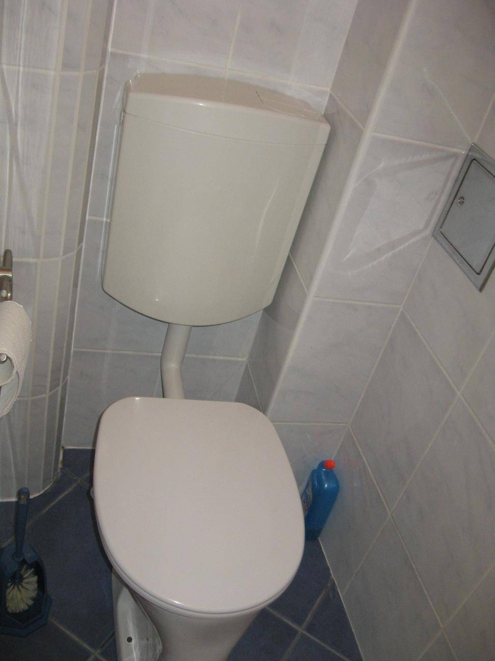 Toilette mit Spülkasten und blauen Bodenfliesen in einem kleinen Badezimmer.