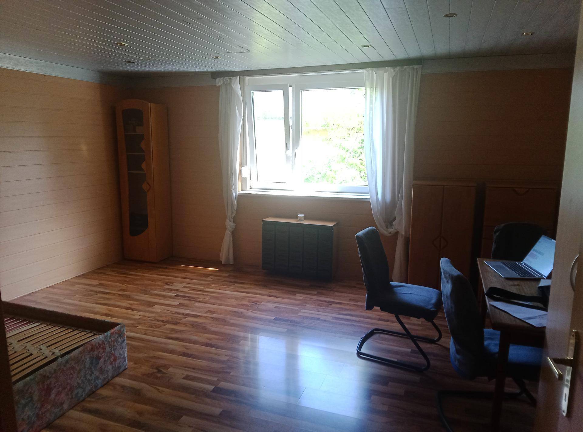 Schlafzimmer mit Laminatboden, Holzvertäfelung und einem Fenster, das einen grünen Ausblick bietet.