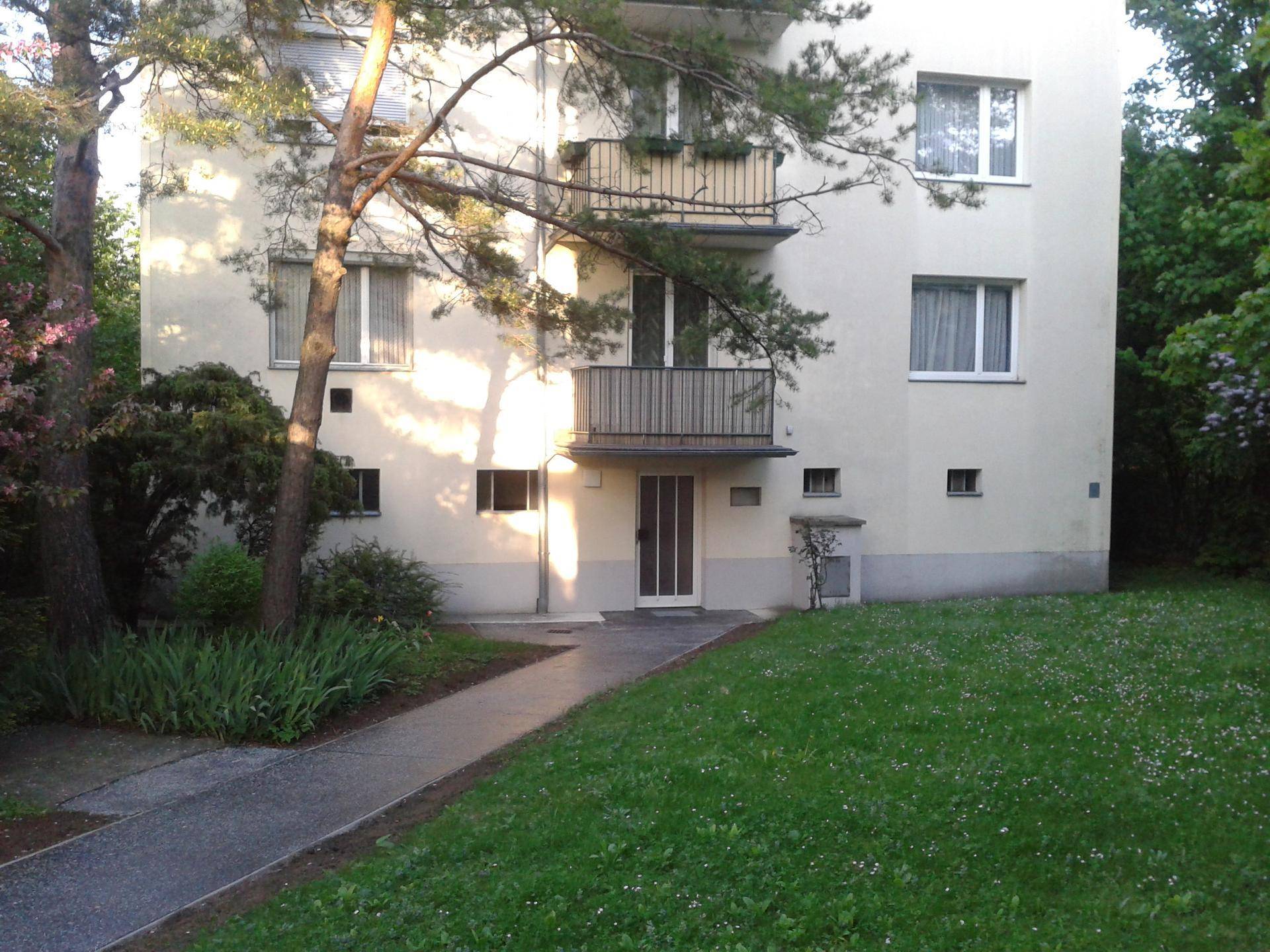 Mehrfamilienhaus mit heller Fassade, Balkonen und einem gepflegten Rasenbereich davor.