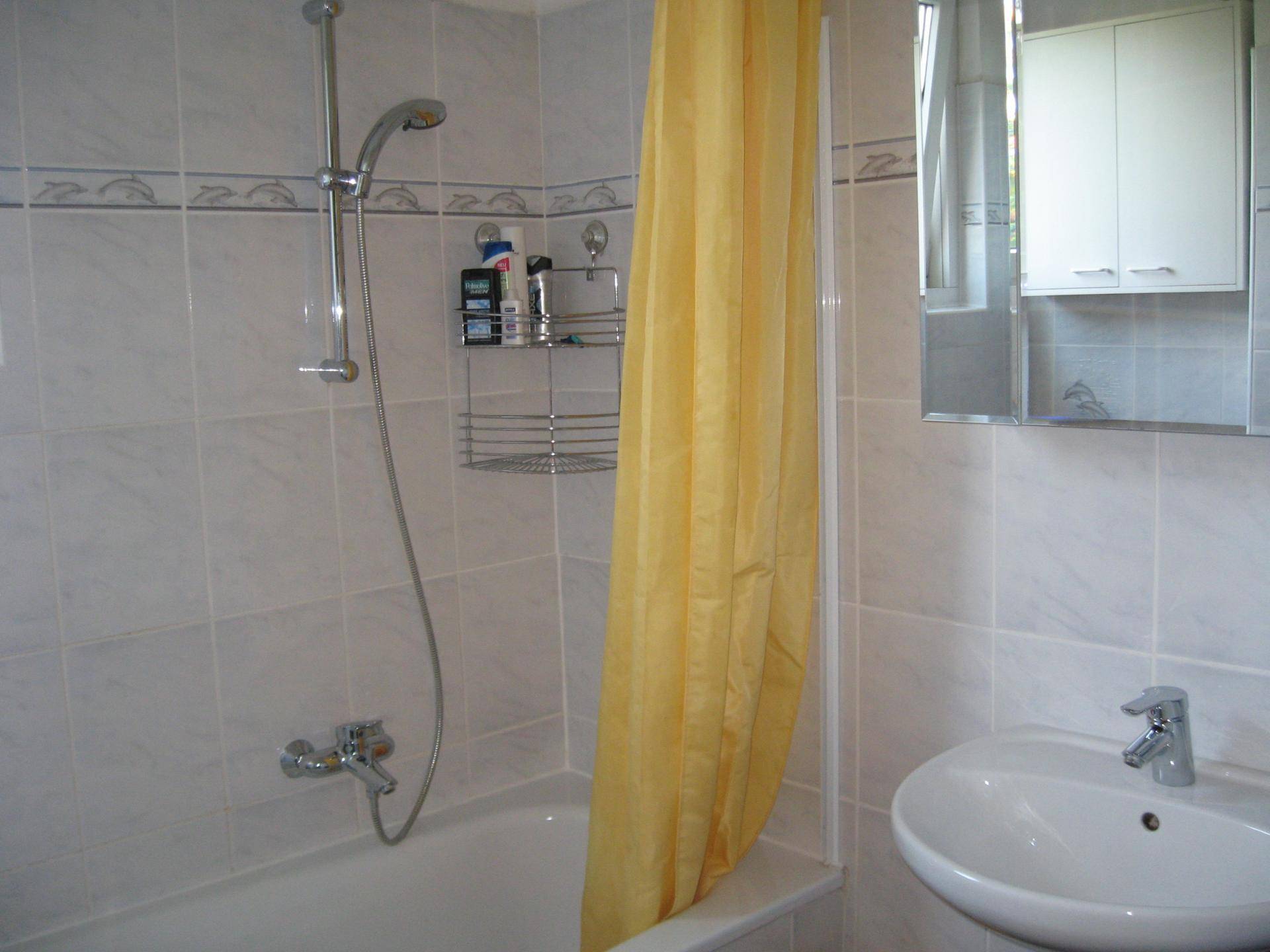 Badezimmer mit Badewanne, Duschvorhang, Waschbecken und hellen Wandfliesen.