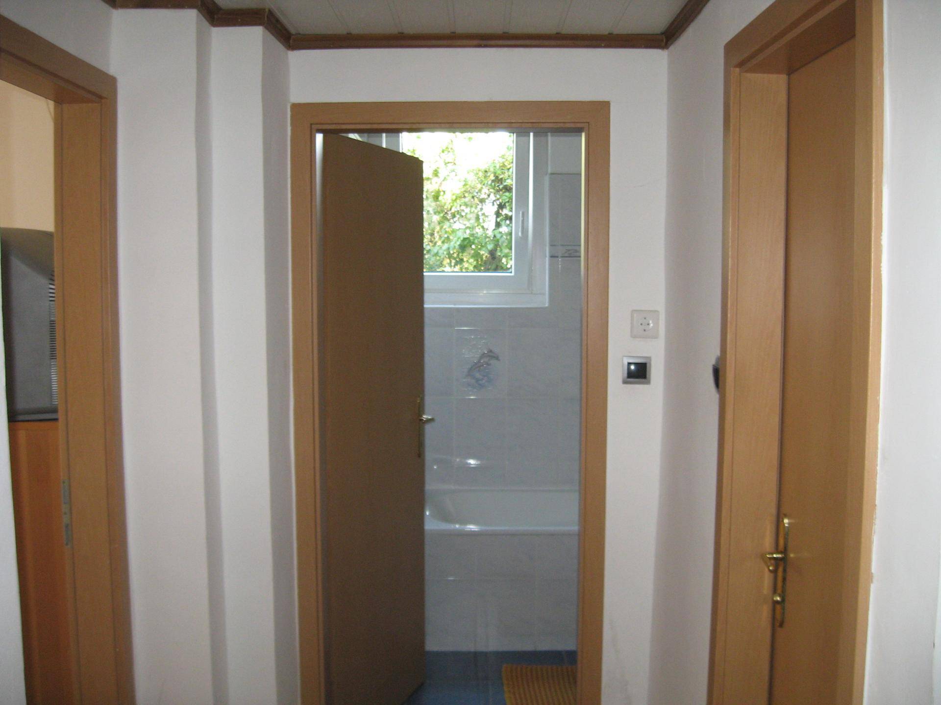 Flur mit Holztüren, der den Blick auf ein Badezimmer mit Fenster freigibt.