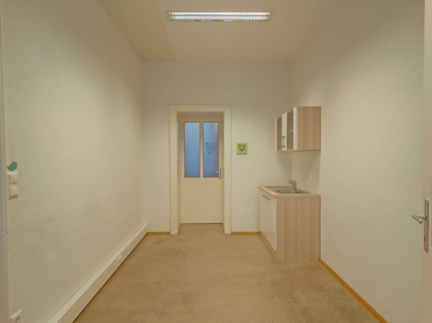 Kleiner Küchenbereich mit Spüle, Unterschrank und Hängeschränken in einem Raum mit Teppichboden.