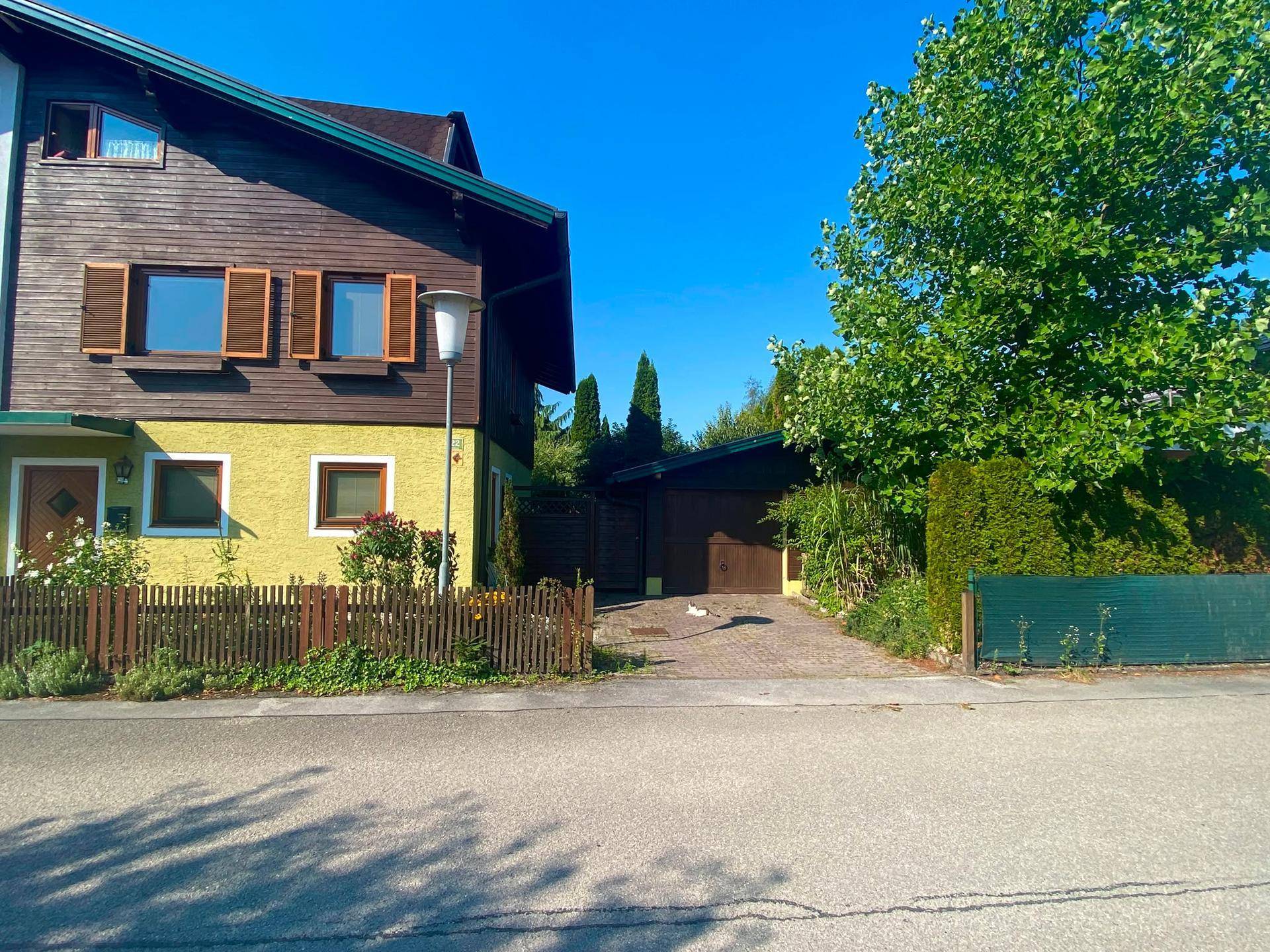 Wohnhaus mit gelber Fassade, Holzverkleidung und Carport-Einfahrt unter klarem Himmel.