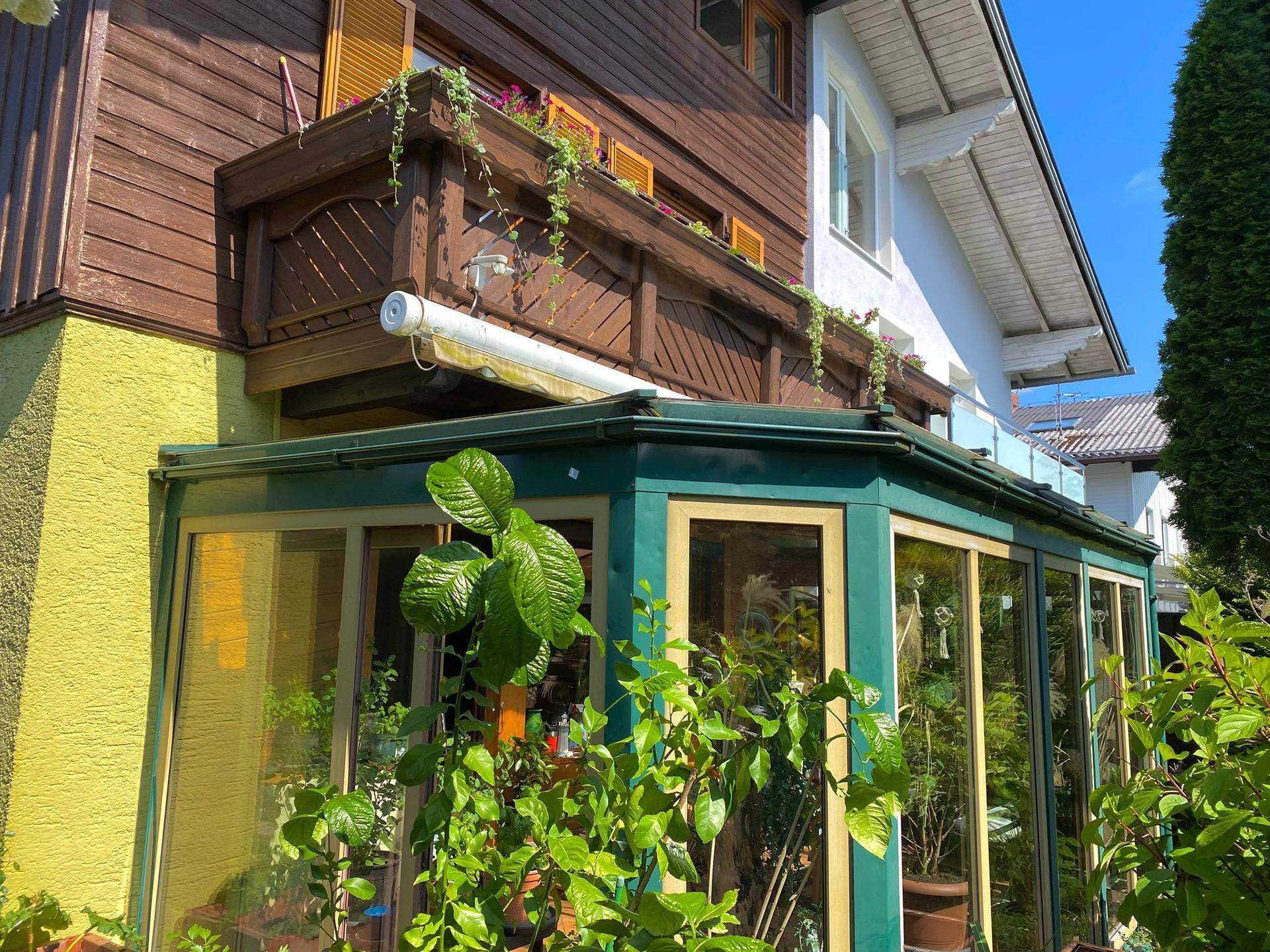 Ansicht des Wintergartens und eines Holz-Balkons an der Hausfassade mit gelbem Anstrich.
