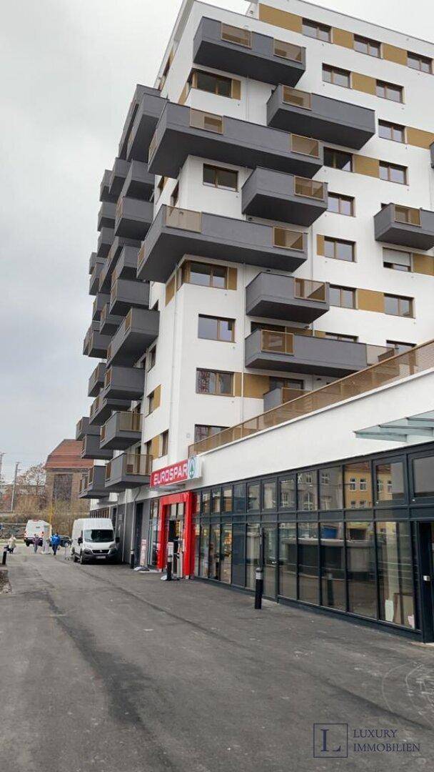 Modernes Wohngebäude mit integriertem Supermarkt im Erdgeschoss an einer städtischen Straße.