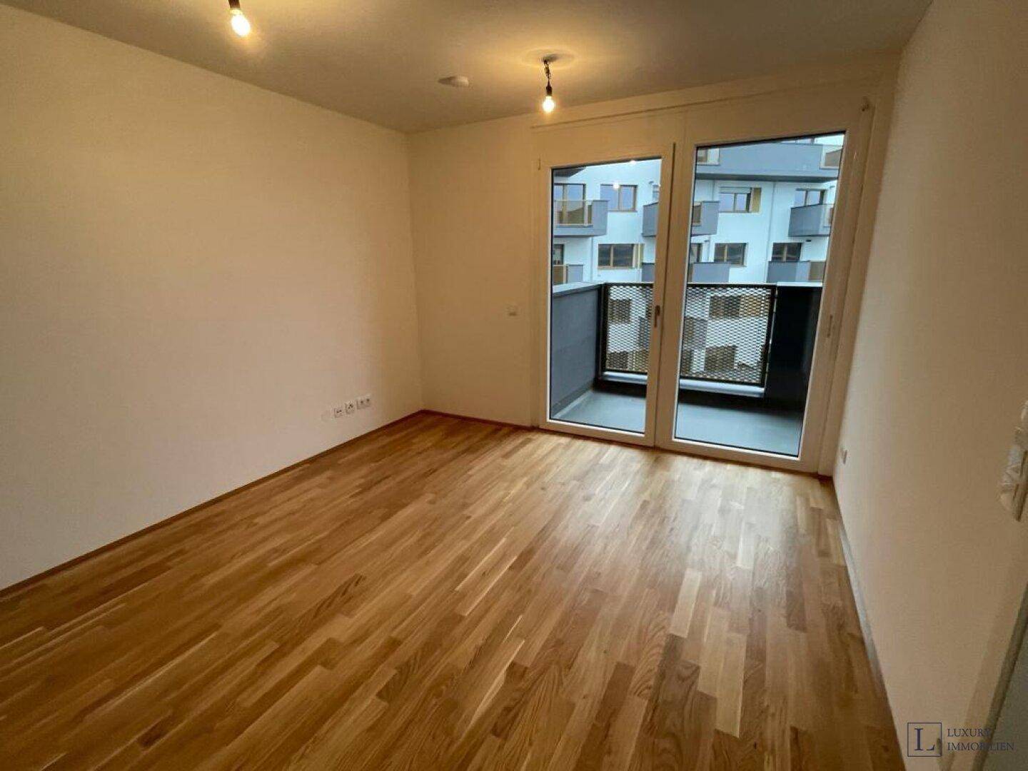 Heller Wohnraum mit Parkettboden und großem Fenster mit Zugang zu einem Balkon.