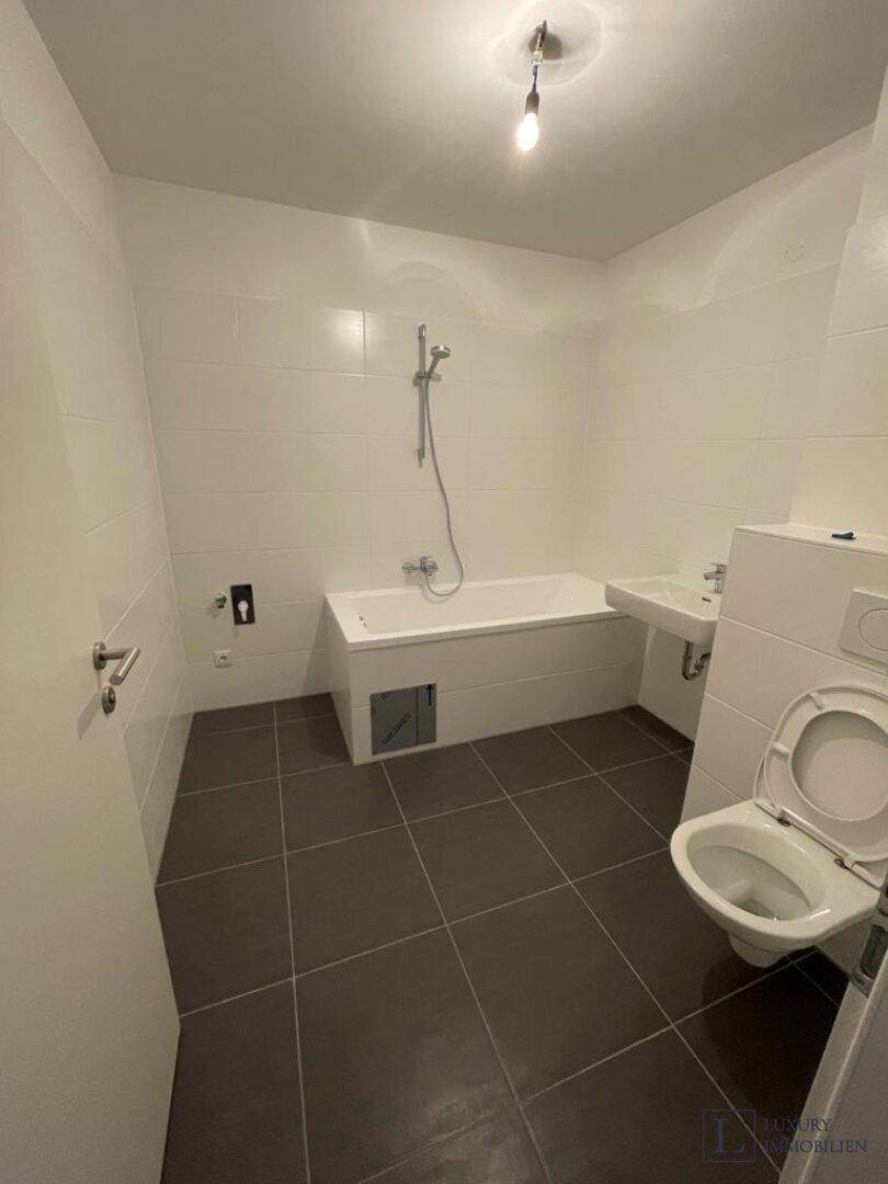 Modernes Badezimmer mit Badewanne, WC und dunklen Bodenfliesen in neuwertigem Zustand.
