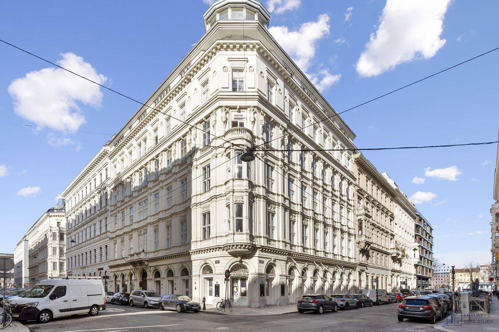 Historisches Eckgebäude mit klassischer Architektur, vielen Fenstern und geparkten Autos auf der Straße.