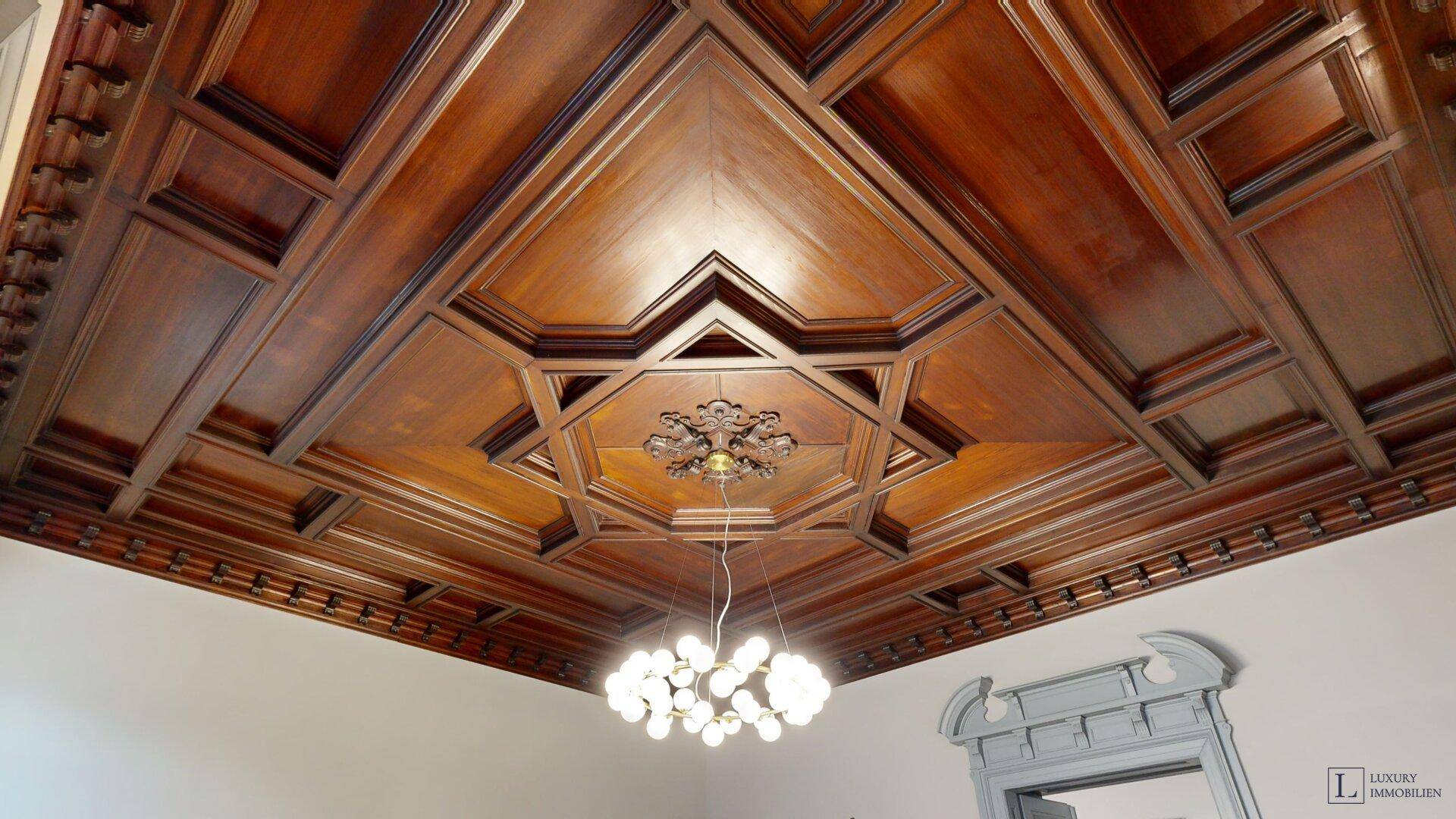 Prunkvolle Holzdecke mit aufwendigen Schnitzereien und einem modernen Kronleuchter.