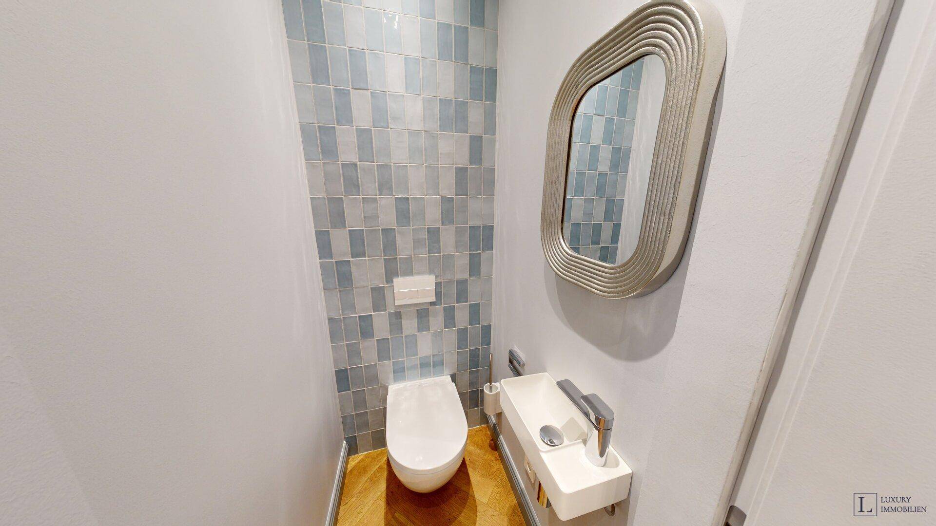 Modernes Gäste-WC mit Wand-WC, kleinem Waschbecken und blauen Fliesen.
