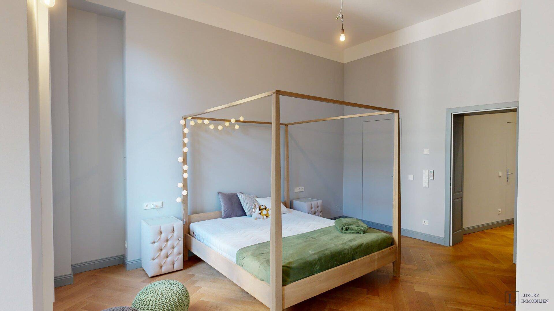 Helles Schlafzimmer mit Himmelbett, Fischgrätparkett und hohen Decken.