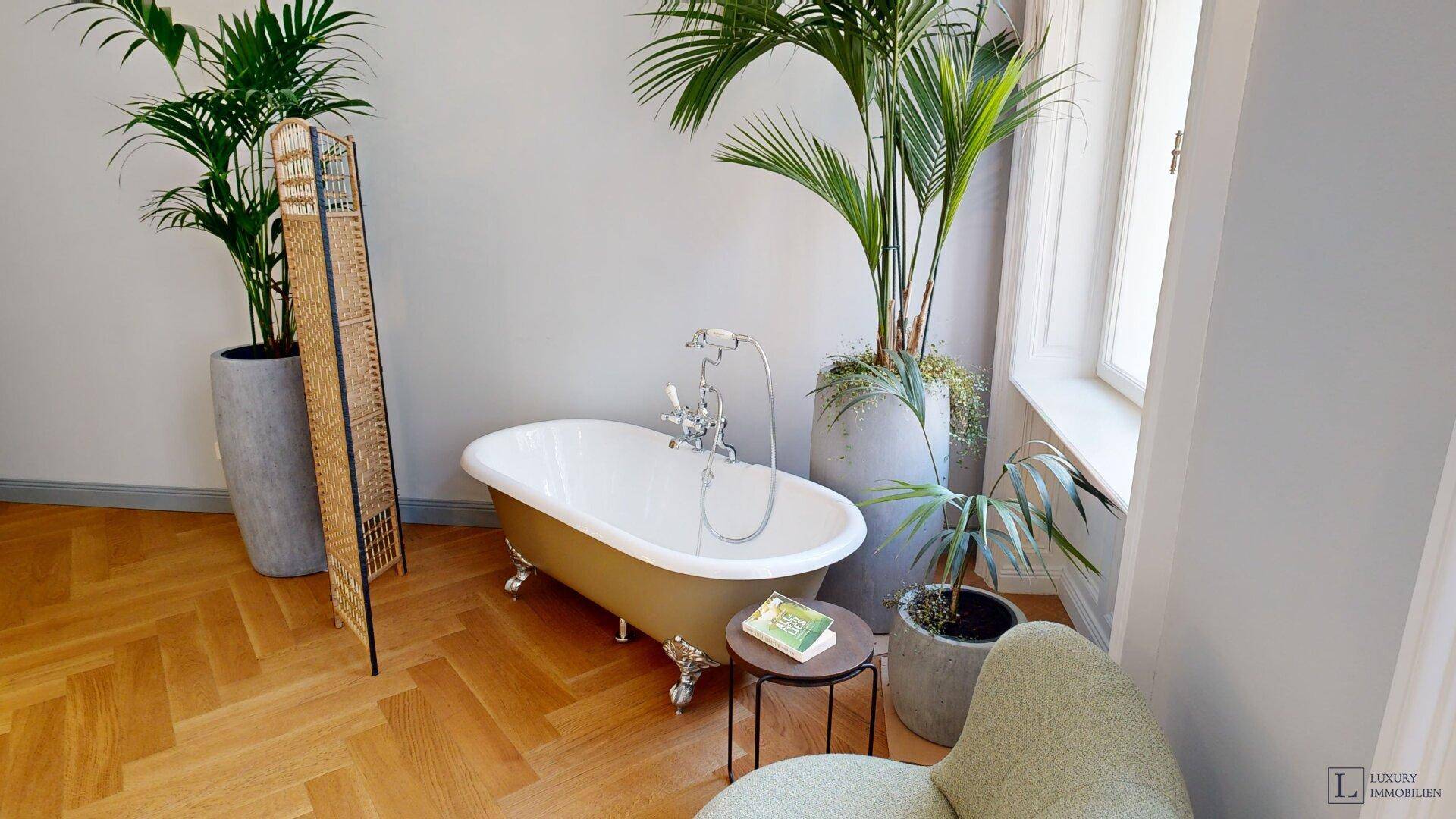 Geräumiges Zimmer mit freistehender Badewanne, Fischgrätparkett und großen Pflanzen.