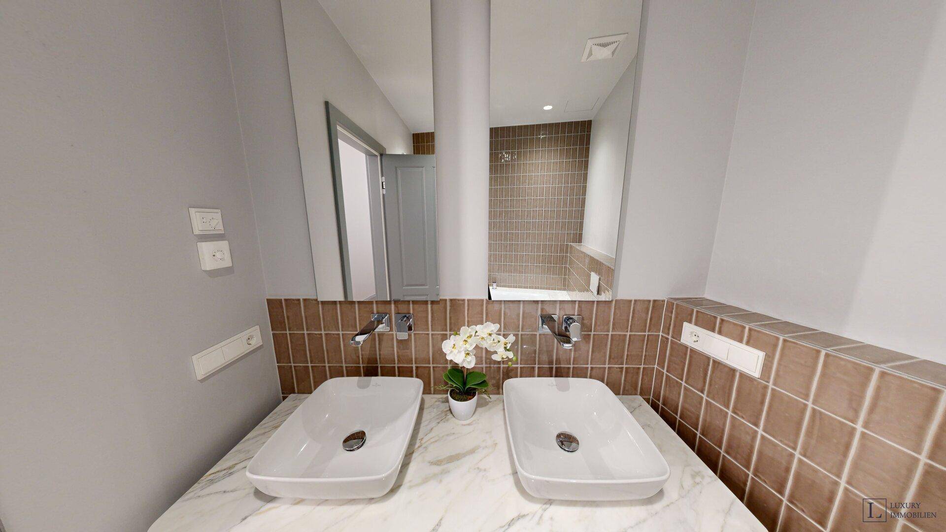 Modernes Badezimmer mit Doppelwaschbecken, großem Spiegel und braunen Fliesen.