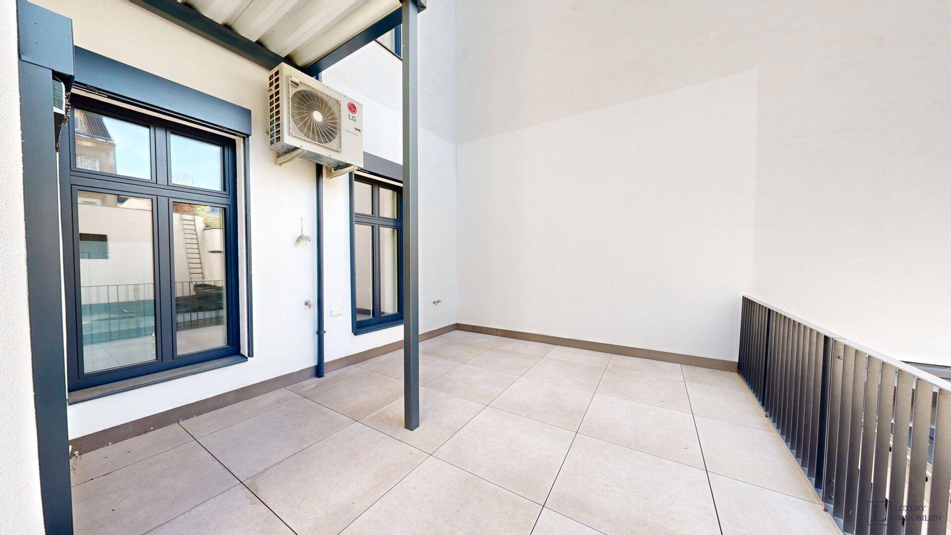 Geräumige Terrasse mit Fliesenboden und Klimaanlage an der Fassade.