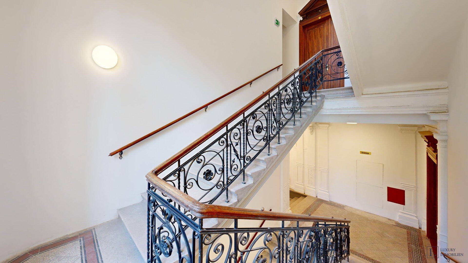 Historisches Treppenhaus mit schmiedeeisernem Geländer und Marmorboden.