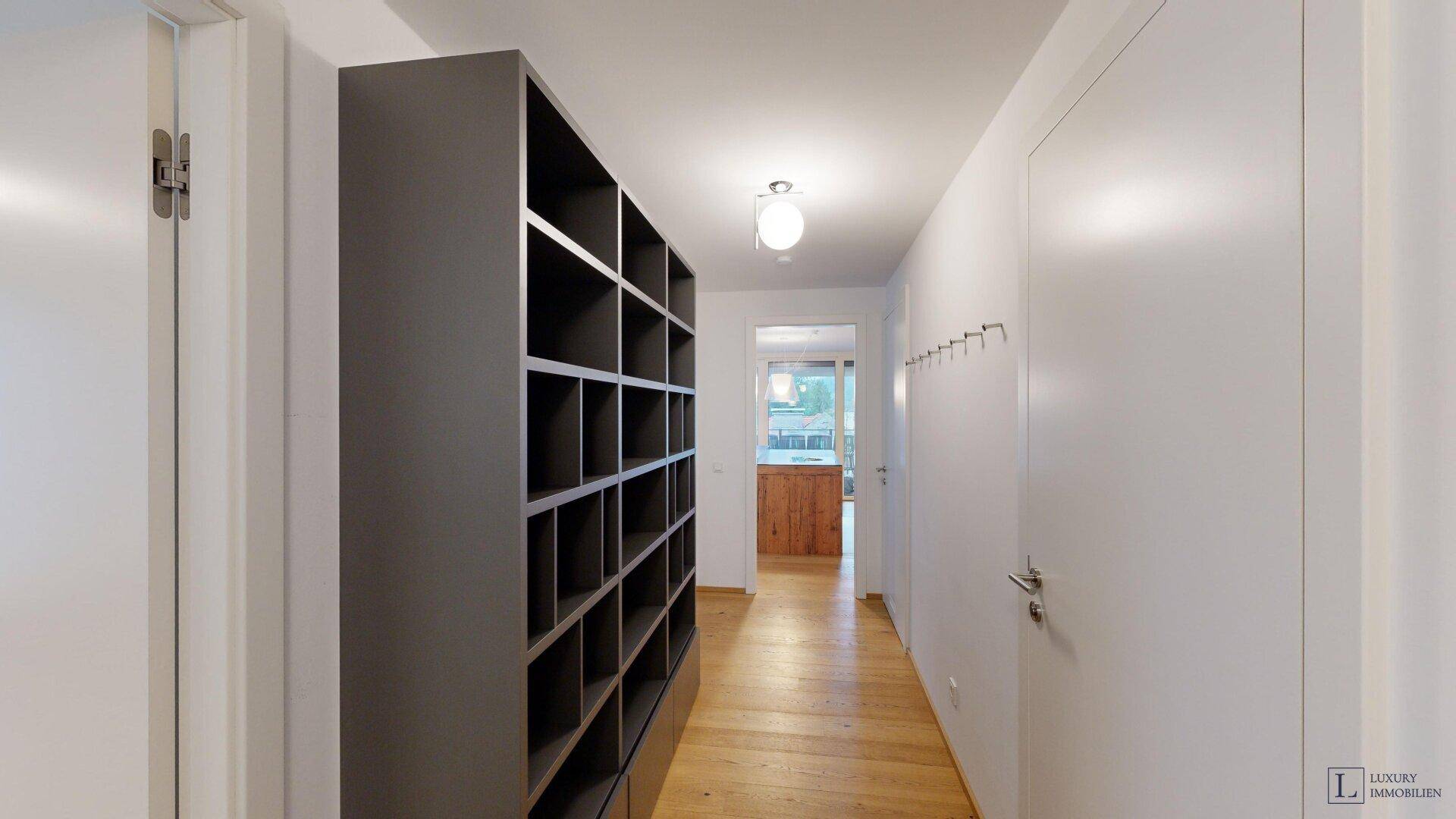 Langer Flur mit Holzboden, Regal und Garderobenhaken.