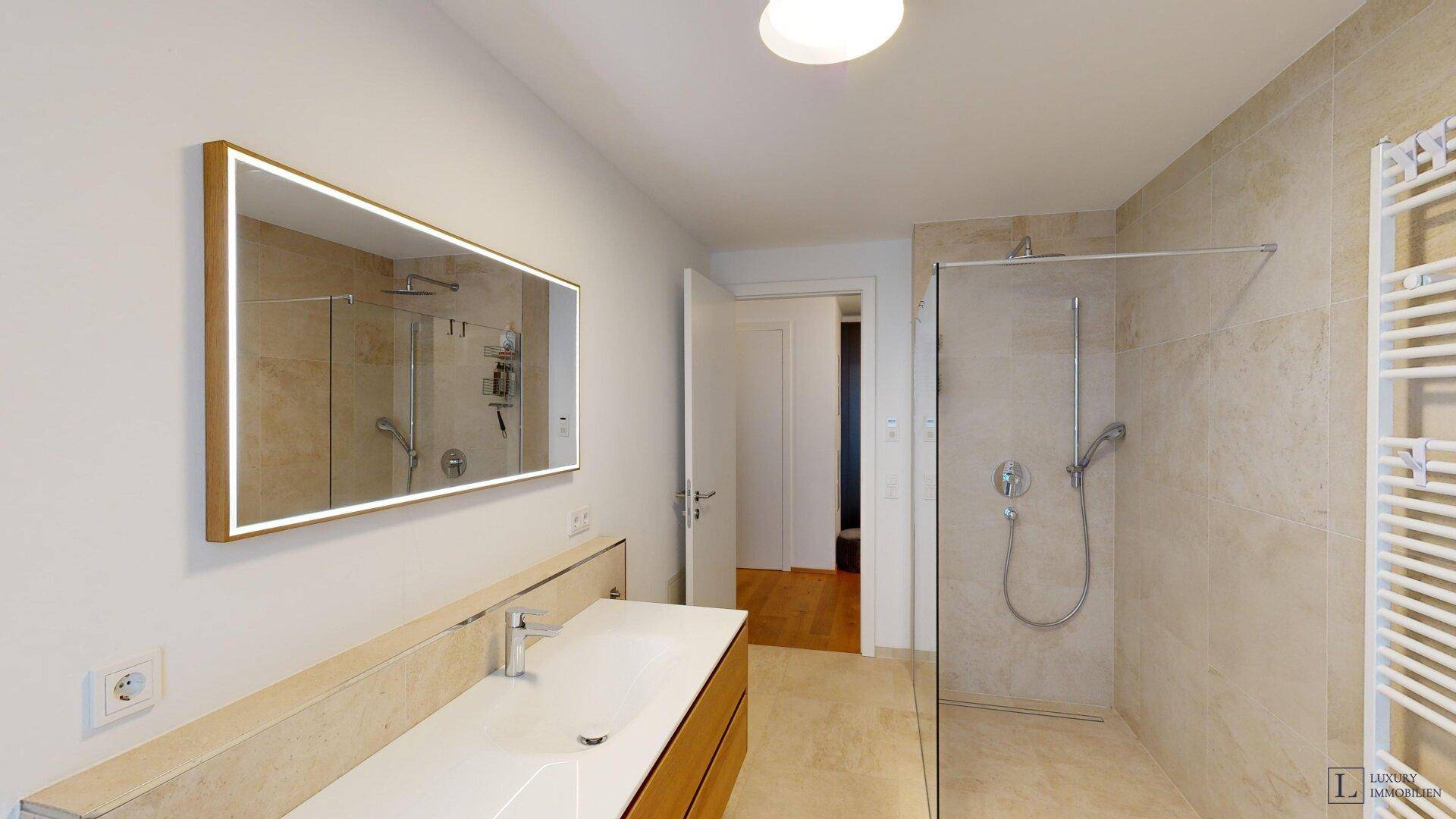 Modernes Badezimmer mit begehbarer Dusche, großem Spiegel und hellen Fliesen.