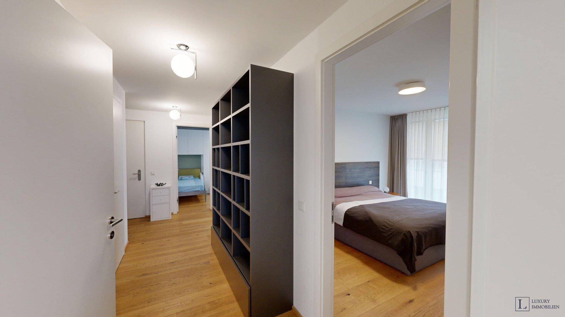 Heller Flur mit Holzboden, Regal und Zugang zu den Schlafzimmern.