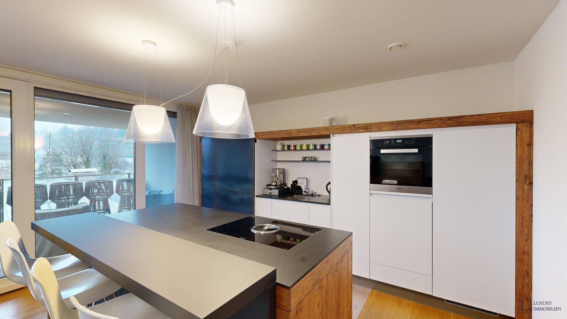 Helle, moderne Küche mit Kochinsel, integriertem Backofen und Zugang zum Balkon.