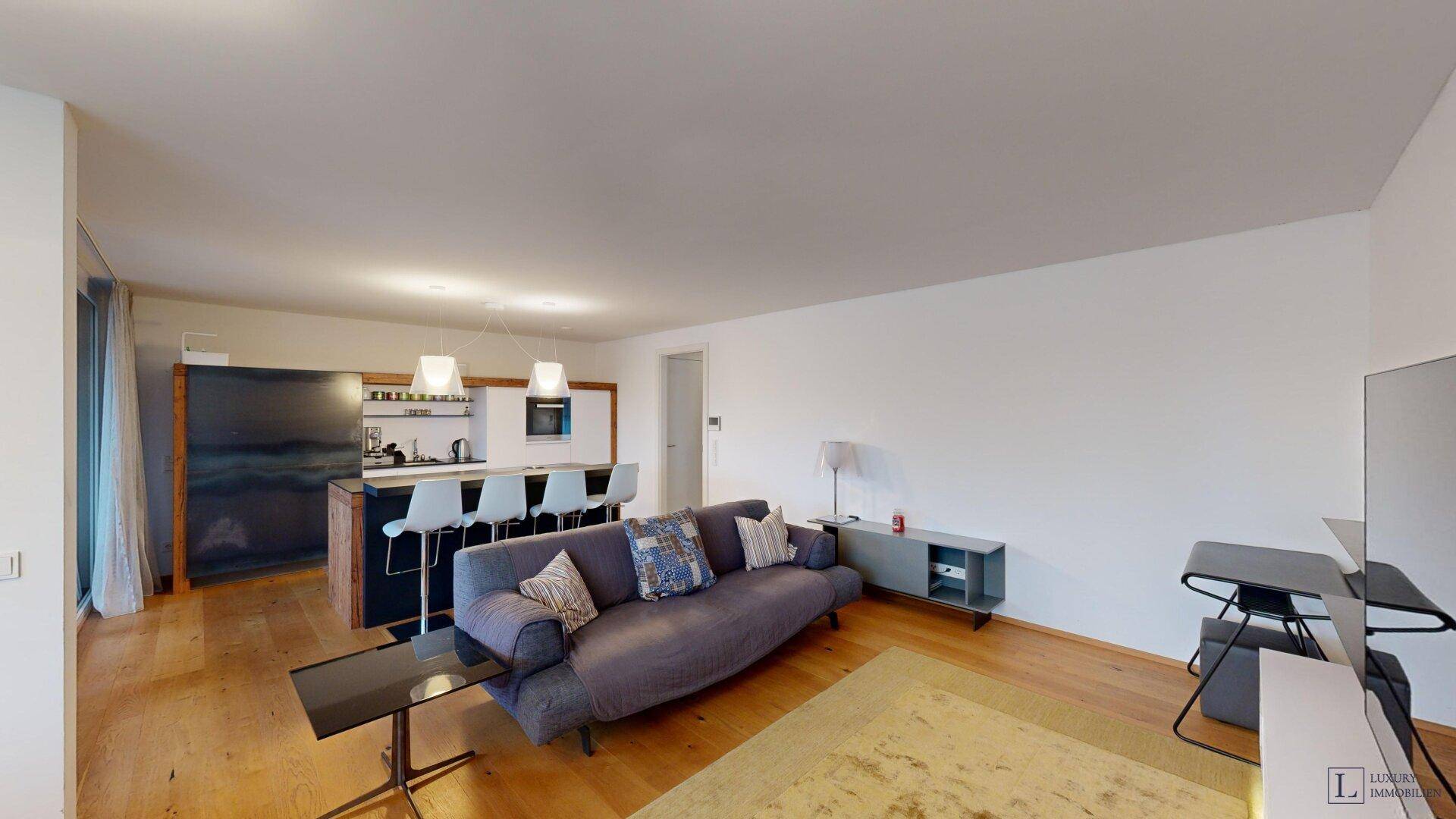 Offener Wohnbereich mit Sofa, integrierter Küche und Holzboden.
