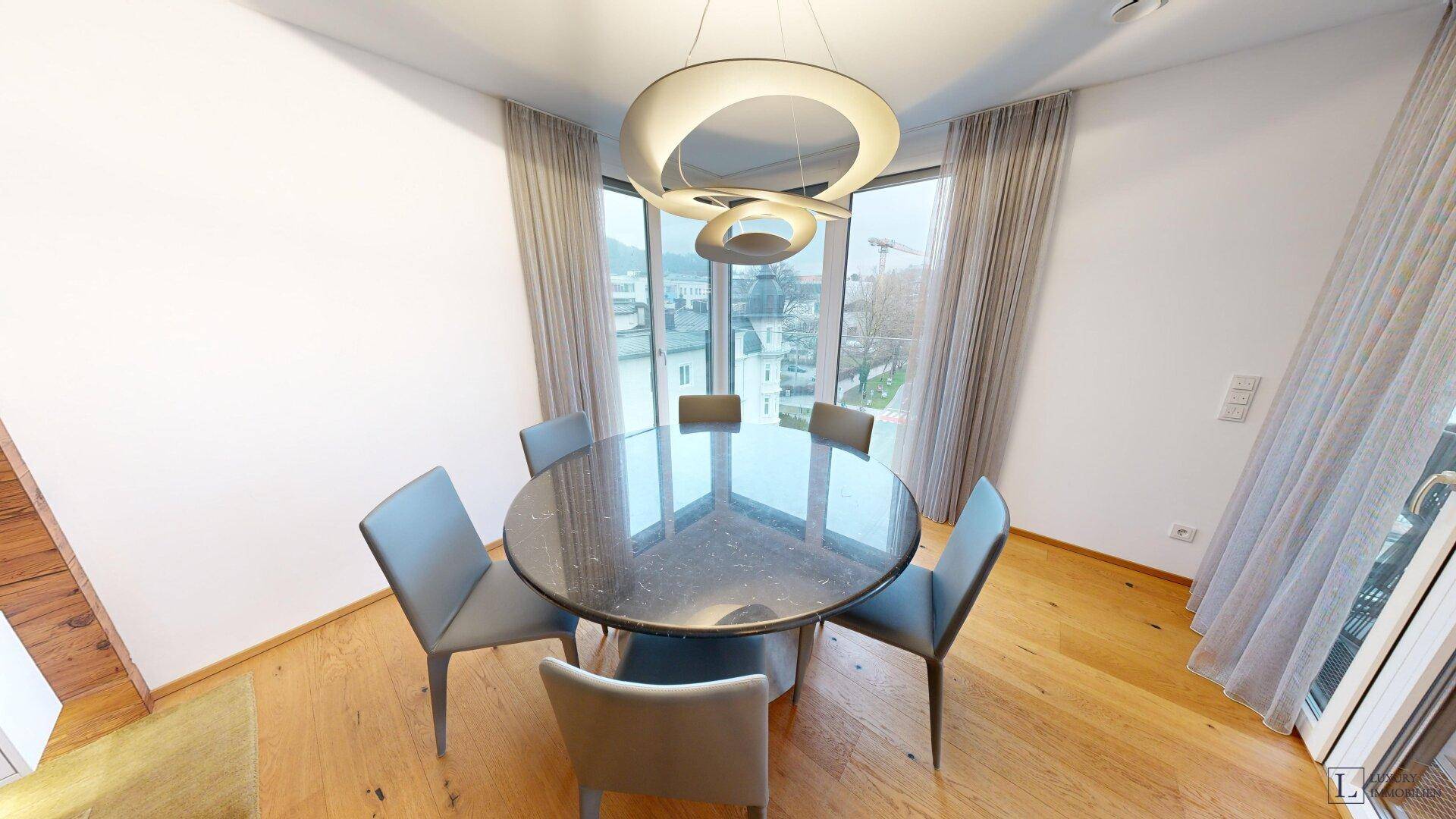 Moderner Essbereich mit rundem Tisch, stilvoller Deckenleuchte und großen Fenstern.