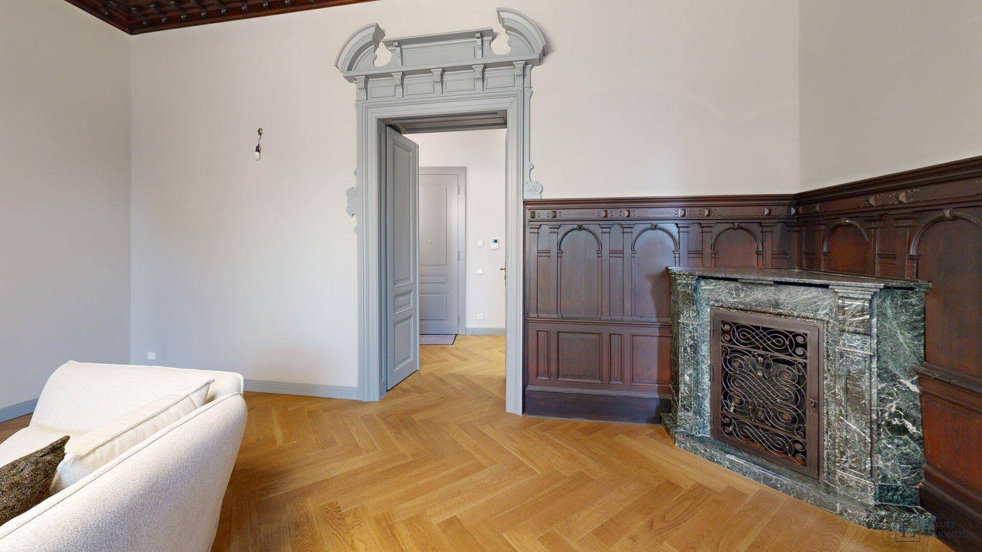 Wohnzimmer mit historischem Kamin, Holztäfelung und Fischgrätparkett.