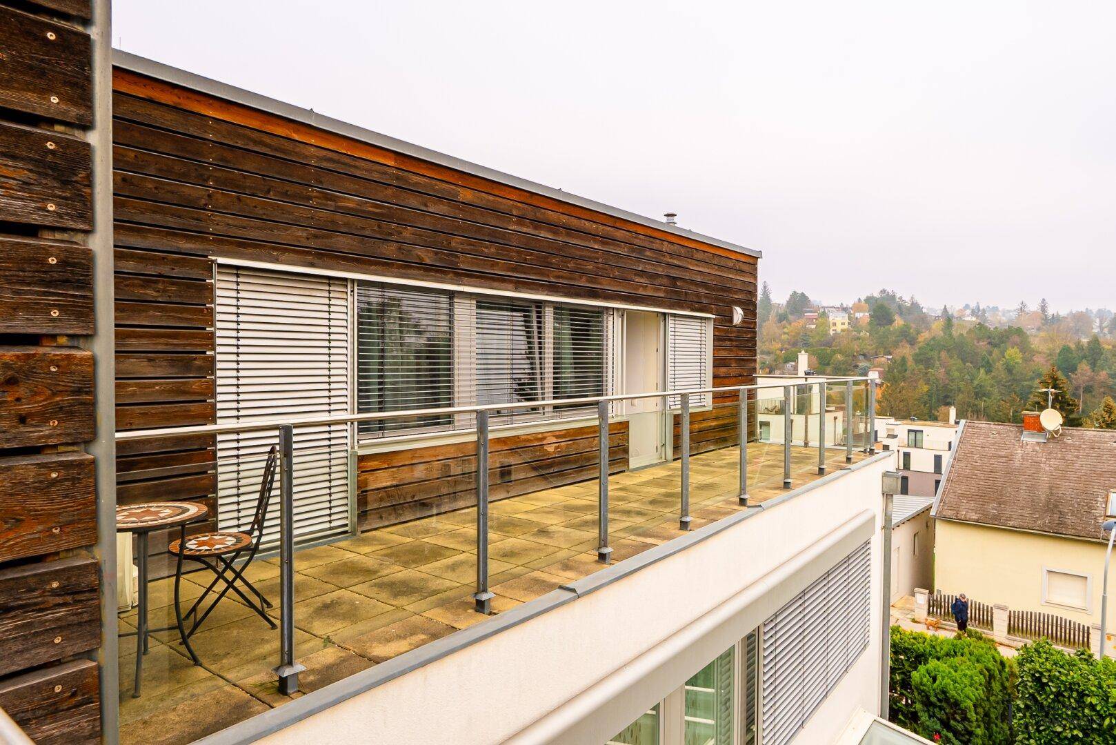 Geräumiger Balkon mit Holzelementen und einem kleinen Tisch, der einen Blick ins Grüne bietet.