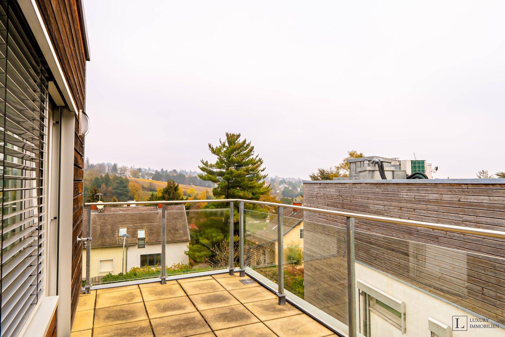 Heller Balkon mit Glasgeländer und weitem Blick über die umliegende Landschaft und Häuser.