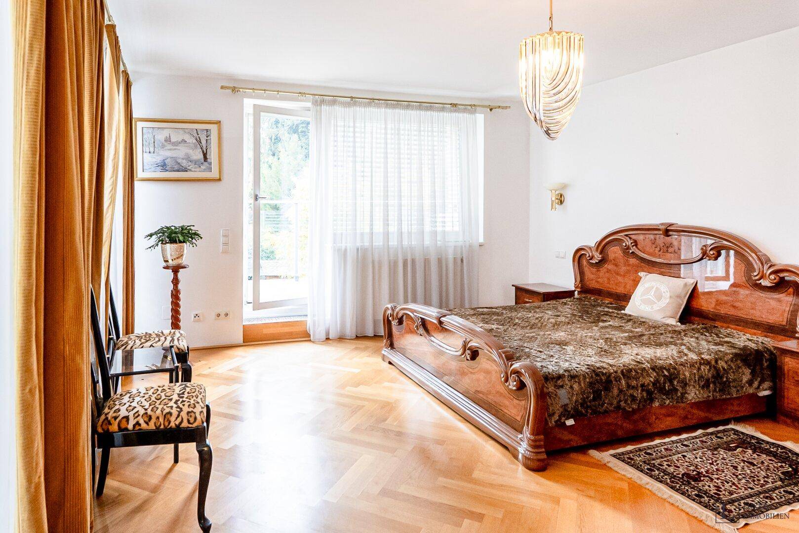 Geräumiges Schlafzimmer mit klassischem Holzdoppelbett, Fischgrätparkett und Balkonzugang.