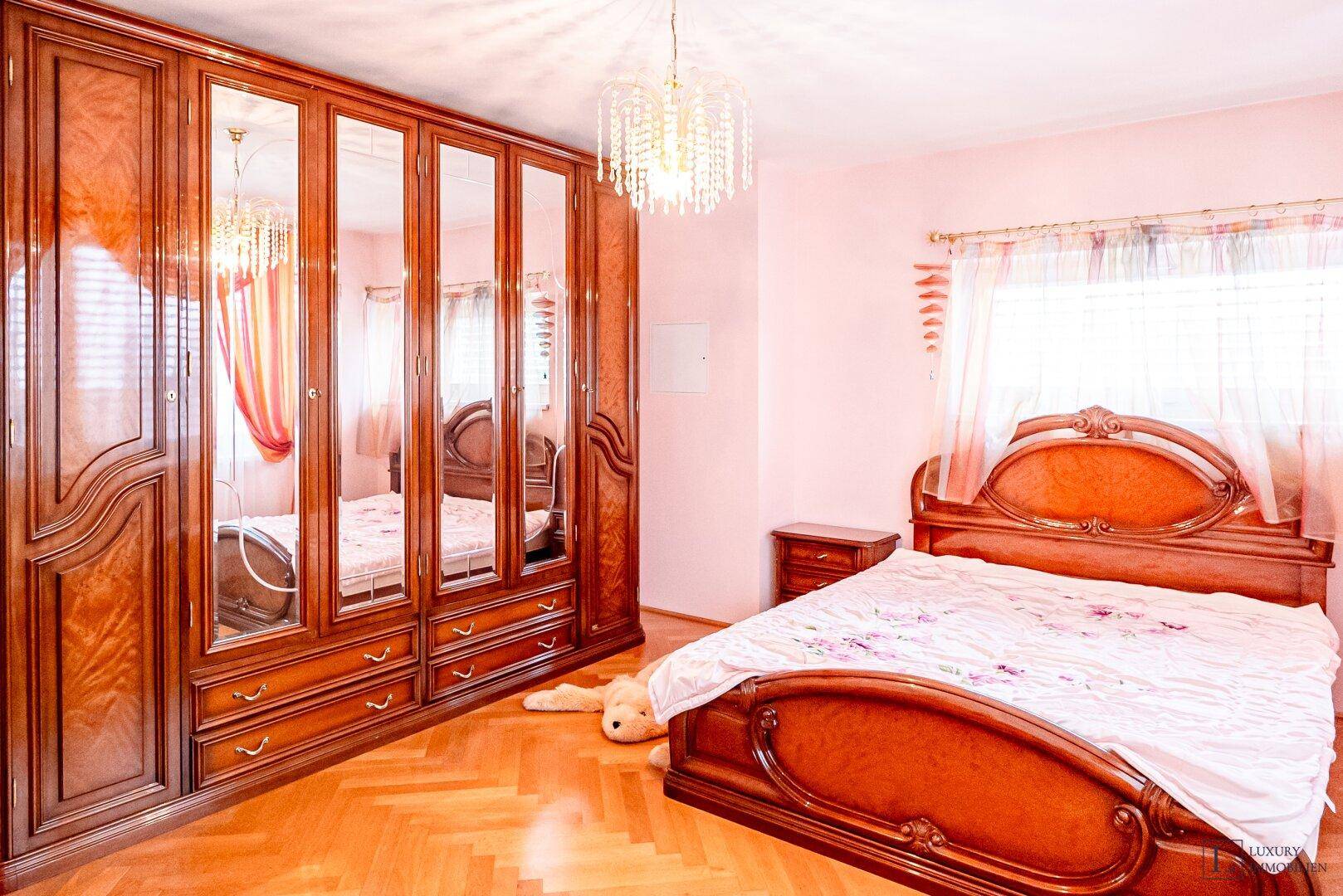 Schlafzimmer mit großem Spiegelschrank, klassischem Holzbett und rosa Wänden.