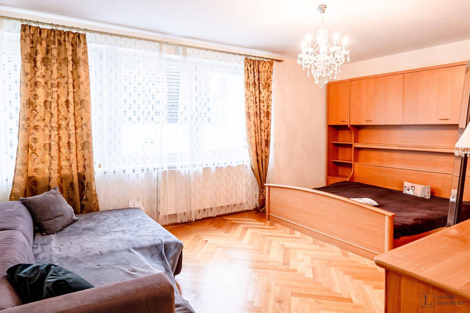 Schlafzimmer mit Einzelbett, Schrankwand und hellem Fischgrätparkettboden.