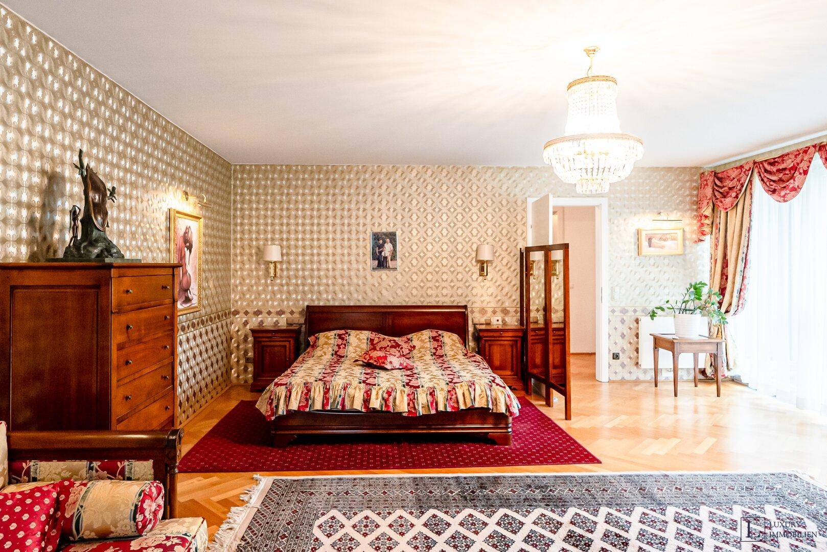 Großes Schlafzimmer mit opulentem Doppelbett, gemusterter Tapete und Kronleuchter.