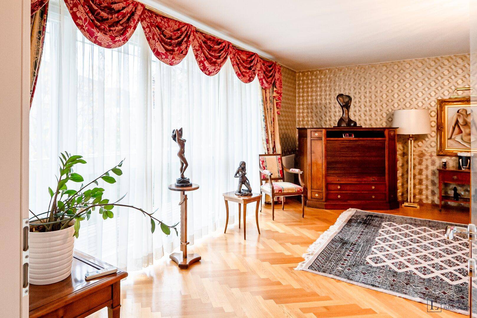 Elegantes Wohnzimmer mit Fischgrätparkett, opulenten roten Vorhängen und klassischen Möbeln.