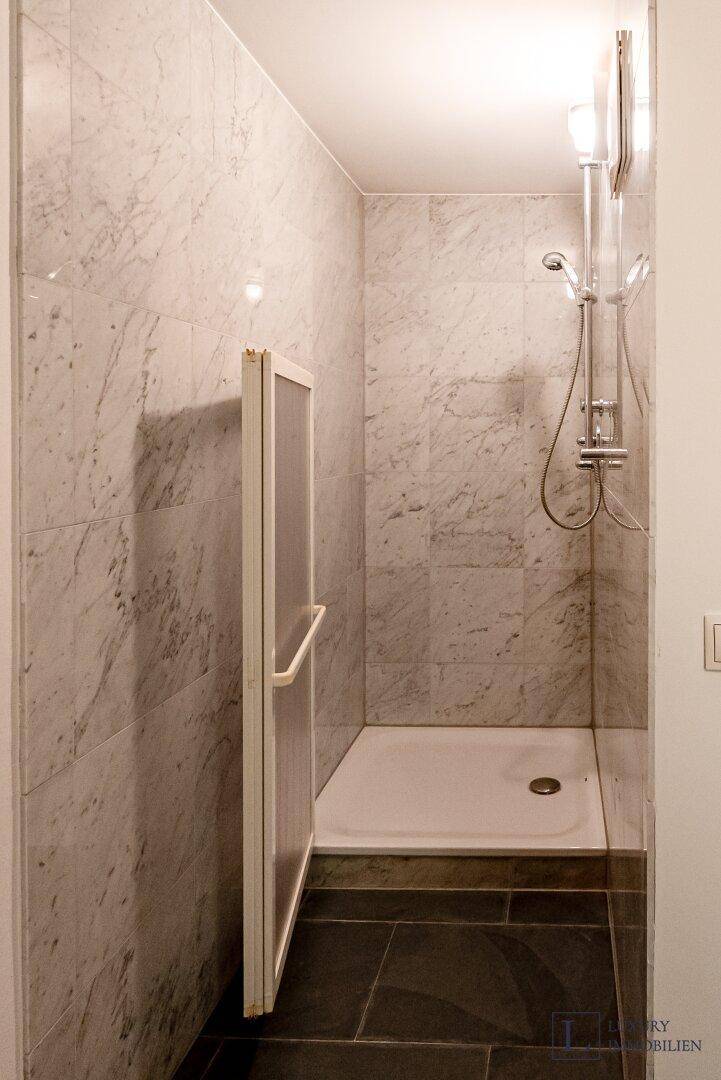 Moderne Dusche mit Marmorfliesen und barrierefreiem Zugang.